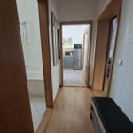 Hallway with view into kitchen, bathroom, and bedroom. Wooden floor and black bench.