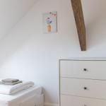 Schlafzimmer mit weißem Bett, Schrank und Holzbalken an der Wand.