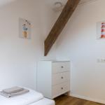 Schlafzimmer mit weißem Schrank, Bett und Holzbalken an der Wand.