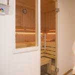 Sauna mit Holzbank und Glasfront. Temperaturanzeige an der Wand.