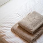 Zwei gefaltete Handtücher liegen auf einem Bett mit weißer Bettwäsche.