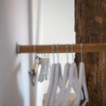 Schrank mit weißen Hängern und Holzstange, neben rustikalem Holzbaumstamm.