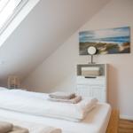Schlafzimmer mit Dachschräge, großem Dachfenster und Bett mit weißen Laken.