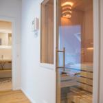 Sauna mit Holzbank und Glaswand. Nebenraum mit Waschbecken und Spiegel.