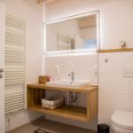 Badezimmer mit Holzwaschtisch, Spiegel und Marmorfliesenboden. Dampfbad und Toilette sind vorhanden.