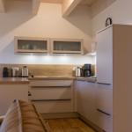 Küche mit Holzoberfläche, Schränken und Kühlschrank. Holzdeckenbalken sichtbar.