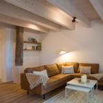 Wohnzimmer mit braunem Sofa, Holzbalken und weißem Tisch.