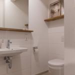 Badezimmer mit Waschbecken, Spiegel, Toilette und Holzregal.