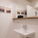 Waschbecken mit Spiegel, Holzregal und Wandbildern