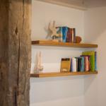 Zwei Holzregale an der Wand mit Büchern und Meeressymbolen. Links Holzpfosten.