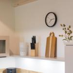 Küchenwand mit Uhr, Messerblock, Schneidebrett und Pflanze.