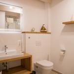 Badezimmer mit Waschbecken, Toilette und Spiegel. Holzakzente und Dachbalken.