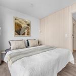 Schlafzimmer mit Bett, Wandbild und Holzwand. Durchgang zu einem weiteren Raum.