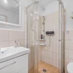 Badezimmer mit Dusche, Waschbecken und Toilette. Fliesenwand und Spiegel.