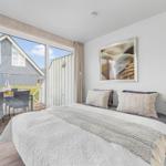 Schlafzimmer mit Balkon, Bett, Wandbild und Pflanze.