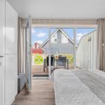 Schlafzimmer mit Balkonblick auf Holzhäuser und Grünflächen.