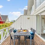 Terrasse mit Tisch und Stühlen, Obst und Wein. Holzdecke, weißer Zaun, Sicht auf Haus und Himmel.