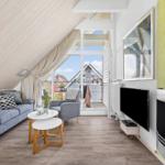 Wohnzimmer mit Sofa, Sessel, Fernseher und Kamin. Blick auf Balkon und Nachbarhäuser.