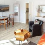 Living room with dining area, sofa, armchair, and TV. Wooden floor and white walls.