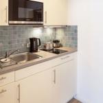Kitchen with sink, stove, and microwave. Tile backsplash and white cabinets.