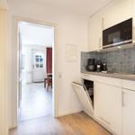 Kitchen with white cabinets, sink, and open dishwasher. Corridor to living area with wooden floor.