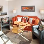 A living room with an orange sofa, two black chairs, and a wooden table.