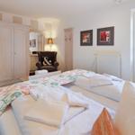 Room with double bed, wardrobe, and armchair. Window with view of outdoor area.