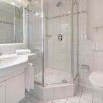 Bathroom with shower, sink, and toilet. Tiles and white sanitary fixtures.