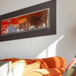 Orange sofa with cushions under an abstract wall picture and a floor lamp.