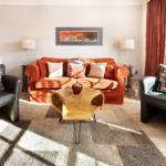 A living room with an orange sofa, two black chairs, and a wooden table.