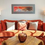A red sofa with cushions, table, lamps, and wall art.