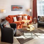 A living room with an orange sofa, two black chairs, and a wooden table.