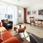 Living room with sofa, armchairs, table, and TV. Windows with curtains and door.