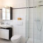 Bathroom with shower, sink, and toilet. White tiles and dark cabinet.