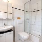 Bathroom with shower, sink and toilet. White tiles and mirror cabinet.