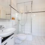 Bathroom with shower, sink, and toilet. White tiles and mirror cabinet.