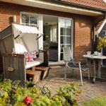 Terrace with lounge chair, table and chairs in front of a house with sliding door.