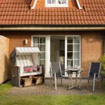 Terrace with lounge, table, and two chairs in front of a house with red roof.