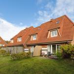 A house with a red tiled roof, garden, and terrace with chair and table.