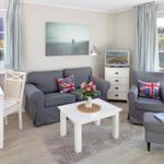 Living room with sofa, armchair, and dining table. Windows with outdoor view.
