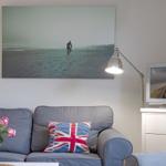 A living room with a sofa, flag-patterned cushions, and a wall picture of a surfer.