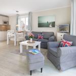 Living and dining area with kitchenette, sofa, and armchair. Windows with view outside.