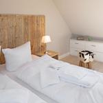 Schlafzimmer mit Holzbett, Nachttisch und Schrank. Fenster und Holzboden sichtbar.