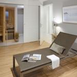 Ein Raum mit Liege, Badewanne und Sauna. Holzfußboden und moderne Einrichtung.
