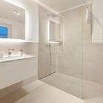 Moderne Badezimmer mit Dusche, Waschbecken und Toilette. Spiegel zeigt Blick auf Meer.