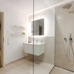 Badezimmer mit Dusche, Waschbecken und Spiegel. Durchgang zur Wohnung.