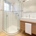 Badezimmer mit Dusche, Waschbecken und Toilette. Holzunterschrank und Spiegel.
