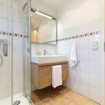 Badezimmer mit Dusche, Waschbecken und Spiegel. Fliesenwand mit Mosaikstreifen.