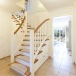 Haus mit Holztreppe und weißen Geländern. Durchgang zu Wohnbereich und Terrasse.