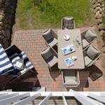 Terrasse mit Tisch, sechs Stühlen und Liegestuhl mit blau-weißem Gestell.